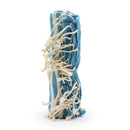 Ein aufrecht stehendes, fest zusammengerolltes Hamamtuch in Blau und Weiß mit dicken, cremefarbenen Fransen, auf weißem Hintergrund.