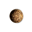 Eine Nahaufnahme von oben einer Metalldose gefüllt mit kleinen, hellbraunen Holzspänen oder Wurzelstücken, wahrscheinlich einer Teezutat wie Süßholzwurzel.