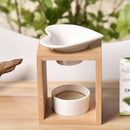 Eine Aromalampe aus Bambusholz mit einer weißen, herzförmigen Keramikschale, platziert neben einer Schachtel Zedernholz-Ätherisches Öl vor einem natürlichen Hintergrund.