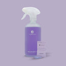 Eine Produktaufnahme auf lavendelfarbenem Hintergrund, die eine durchscheinende, mattierte Sprühflasche für COSMEAU MEHRZWECK-REINIGER mit einer lila Flüssigkeit zeigt. Vor der Flasche liegt ein einzelner versiegelter Folienbeutel mit MEHRZWECK LAVENDEL Reinigungs-Tabs und einer passenden lila, sprudelnden Tablette im Vordergrund.