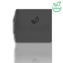 Quadratisches Stück dunkler veganer Seife mit Blatt-Logo, auf einer reflektierenden weißen Oberfläche.