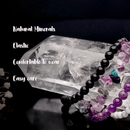 Mehrere Armbänder aus dunklen und violetten Perlen vor einem großen, durchsichtigen Stein.