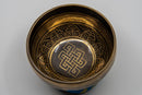 Nahaufnahme des Inneren einer dunklen Metall-Klangschale, die aufwendige goldene Gravuren und das zentrale Symbol des Endlosen Knotens zeigt.
