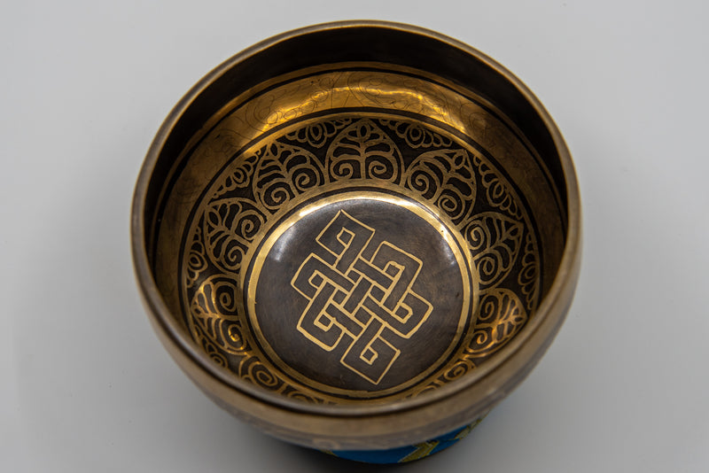 Nahaufnahme des Inneren einer dunklen Metall-Klangschale, die aufwendige goldene Gravuren und das zentrale Symbol des Endlosen Knotens zeigt.