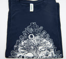 Ein gefaltetes, marineblaues T-Shirt mit einem detaillierten weißen Aufdruck eines Tannenzapfens, dessen Schuppen eine Miniaturlandschaft mit einem zentralen Baum umschließen.