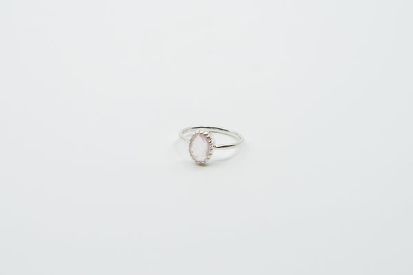 Ein silberner Ring mit einer schlichten Ringschiene und einem ovalen, facettierten Stein, der von einem zarten gewellten Rand umgeben ist, auf einem weißen Hintergrund.