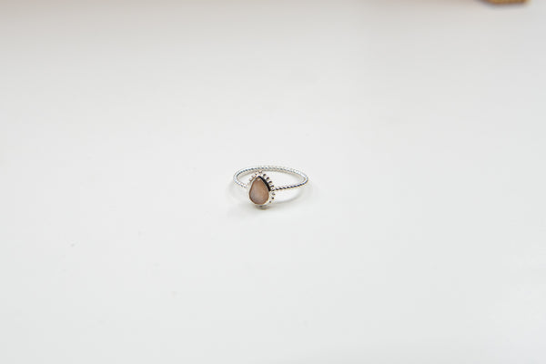 Ein silberner Ring mit gedrehter Ringschiene und einem birnenförmigen, hellbraunen Stein, auf einem weißen Hintergrund.