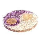 Eine Yin-Yang-Scheibe aus lila und weißen Steinen mit goldenen, geometrischen Mustern.