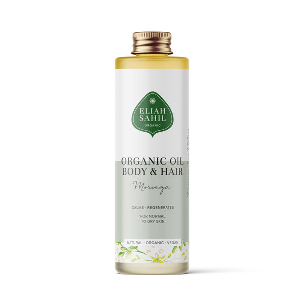Produktfoto einer hohen weißen Flasche „Eliah Sahil Organic Oil Body & Hair Moringa“ mit einem hellgrünen Etikett, das besagt, dass es normale bis trockene Haut beruhigt und regeneriert.
