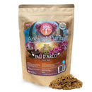 Ein brauner Papierbeutel mit "Ancient Purity Pau D'arco (Inner Bark)" und einem farbenfrohen Etikett, das einen alten Maya- oder Aztekenkalender und rosa Blumen zeigt. Ein Haufen der inneren Rinde liegt vor dem Beutel.