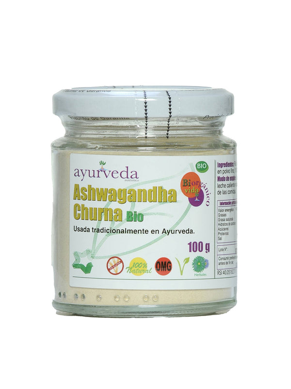 Ein Glasgefäß mit "Ayurveda autentico Ashwagandha Churna Bio" auf weißem Hintergrund. Das Vorderetikett zeigt den Produktnamen, "Usada tradicionalmente en Ayurveda" (traditionell in Ayurveda verwendet) und Zertifizierungen für "Sin Gluten", "100% Natural", "OMG" (gentechnikfrei) und "100 g".