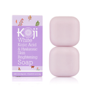 Eine violette Schachtel mit der Aufschrift „Koji White Kojic Acid & Hyaluronic Skin Brightening Soap“ neben zwei gestapelten blassrosa Seifenstücken vermittelt ein frisches, sauberes Gefühl.