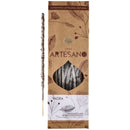 Ein handgefertigtes, natürliches Yagra-Räucherstäbchen neben der Verpackung der Sagrada Madre Línea Artesano. Die braune Schachtel, verziert mit Blattillustrationen, hat ein Sichtfenster zu den Stäbchen und betont den Zweck: „Fülle und zieht Wohlstand an“ (Abundancia y Atrae Dinero).