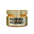 Ein kleines Glas ANUK Manuka Honig MGO 250 mit einem goldenen Etikett, isoliert auf weißem Hintergrund.