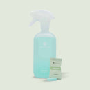 Eine Studioaufnahme, die eine durchscheinende, mattierte Sprühflasche für COSMEAU KÜCHENREINIGER mit einer hellblauen Flüssigkeit zeigt. Vor der Flasche befindet sich ein versiegelter Folienbeutel mit KÜCHE ZITRONE Reinigungs-Tabs und einer einzelnen hellblauen, sprudelnden Tablette im Vordergrund.