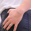 Nahaufnahme der Hand einer Person, die zwei silberne Diamantringe und ein funkelndes Bolo-Armband trägt.