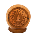 Eine runde, geschnitzte Salzlampe mit einem Buddha- und Mandala-Motiv in Holzrahmen auf einem dunklen Holzsockel.