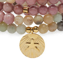 Eine Nahaufnahme eines Stapels von drei Perlenarmbändern aus runden rosa, cremefarbenen und hellgrünen Edelsteinperlen (wahrscheinlich Rhodonit/Amazonit). Die Armbänder sind mit goldfarbenen Metall-Abstandshaltern und einem großen runden Goldmedaillon-Anhänger mit zentralem Stern und radialen Linien verziert.