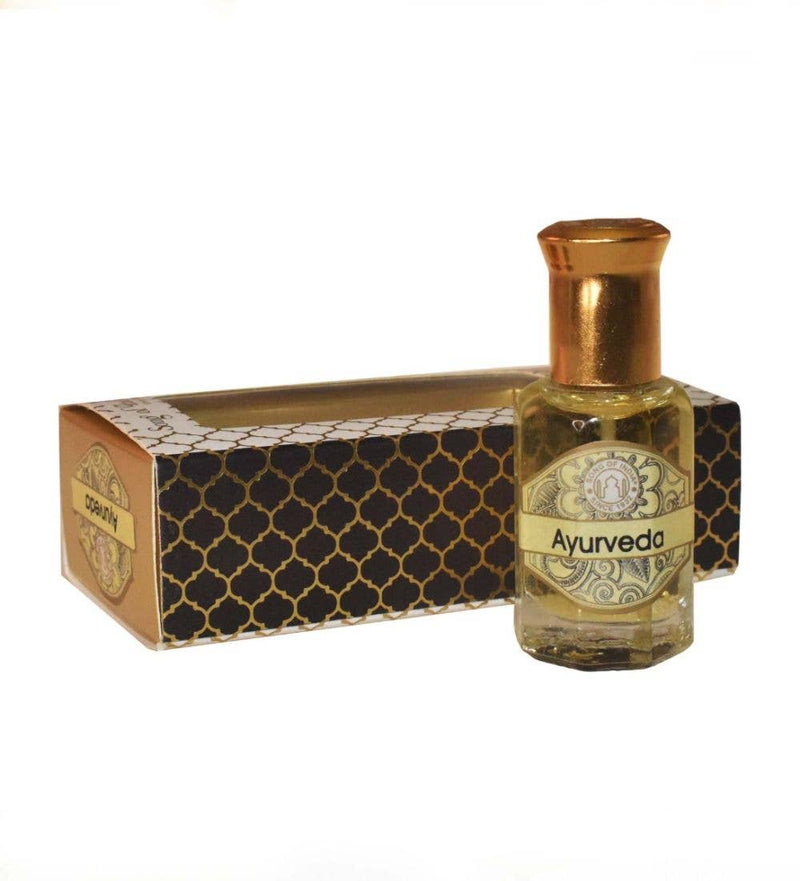 Kleines Glasfläschchen mit gelbem ätherischem Öl und der Aufschrift „Ayurveda“ neben seiner schwarz-gold gemusterten Präsentationsbox vor weißem Hintergrund.