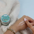 Hand trägt Aumyana Gel-Crème Aloha Feuchtigkeitscreme neben dem Tiegel auf.