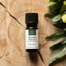 Eine kleine Flasche Pfefferminz-ätherisches Öl auf einer Holzscheibe mit grünen Blättern.