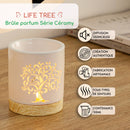 Produktbild einer beleuchteten, weißen Keramik-Duftlampe mit ausgeschnittenem Lebensbaum-Design und Holzsockel. Der Text hebt Merkmale wie „Geräuschlose Diffusion“ und „50 ml Fassungsvermögen“ hervor.