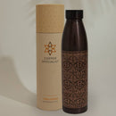 Verzierte dunkle Kupfer-Wasserflasche, die neben ihrer zylindrischen Verpackungshülle mit der Aufschrift „Copper Specialist“ steht.