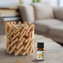 Eine Flasche des ätherischen Öls Zen'Arôme Tea Tree steht auf einem Holztisch neben einem rustikalen Kerzenhalter aus ineinandergreifenden hellen Holzstäbchen.