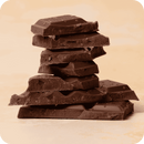 Ein unregelmäßiger Stapel von rechteckigen dunklen Schokoladenstücken, die lose übereinander liegen, vor einem hellbeigen Hintergrund.