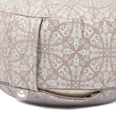 Nahaufnahme eines beigen Meditationskissens mit weißem Ornamentmuster, plissierten Seiten, sichtbarem Reißverschluss und Logo-Etikett, auf weißem Hintergrund.