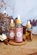 Drei kleine Flaschen mit Pipetten und goldener Flüssigkeit, die als "Freya" gekennzeichnet sind, stehen auf einem Holzscheit, umgeben von getrockneten Pflanzen und Zimt.

