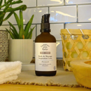 Eine Flasche Massageöl mit Kokosnuss-Inspiration mit schwarzem Pumpspender auf einer Theke mit Pflanzen und Handtüchern.