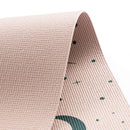 Eine Nahaufnahme einer hellrosa Kinder-Yogamatte, die gebogen ist, um ihre strukturierte Oberseite und das petrolfarbene Grafikdesign der Unterseite mit Punkten und einer Mondform zu zeigen.