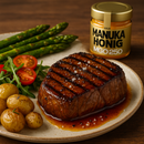 Ein gegrilltes Steak, kleine Kartoffeln, Spargel und ein kleiner Salat neben einem Glas Manuka-Honig.