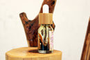 A "Self Love perfume oil" bottle with a bamboo cap and dropper stands prominently on a light wooden surface. The golden oil inside is infused with visible botanical elements, reflecting the natural and mindful nature of the product.