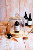 Eine einzelne Flasche Lion's Mane Flüssigextrakt unter einer kleinen Glaskuppel mit einer goldenen Quaste und einem Löffel auf einem Holzhintergrund.