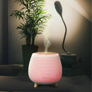 Beleuchteter Aroma-Diffusor in Streifenmuster, der Dampf abgibt, neben einer Zimmerpflanze und einer Schreibtischlampe.