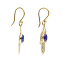 Seitenansicht eines Paares goldfarbener Hamsa-Hand-Ohrhänger, die die Dicke der ovalen Lapislazuli-Edelsteine hervorhebt.