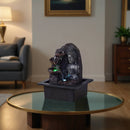 Ein beleuchteter Buddha-Zimmerbrunnen auf einem Couchtisch mit Glasplatte in einem gemütlichen Wohnzimmer.