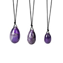 Ein Set aus drei polierten lila Amethyst Steineiern in verschiedenen Größen, die jeweils an einer schwarzen Schnur hängen.