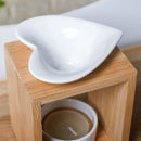 Eine Nahaufnahme der Oberseite einer Aromalampe aus Bambus, die die weiße, herzförmige Keramikschale und den Teelichthalter darunter zeigt.