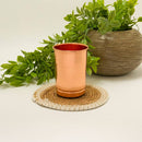 Glänzender Kupferbecher auf einem geflochtenen Untersetzer neben einer Topfpflanze