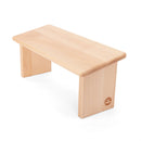 Helle Buchenholz-Meditationsbank mit glatter rechteckiger Sitzfläche und zwei massiven Beinen, dezente Logo-Gravur an einem Bein, auf weißem Hintergrund.