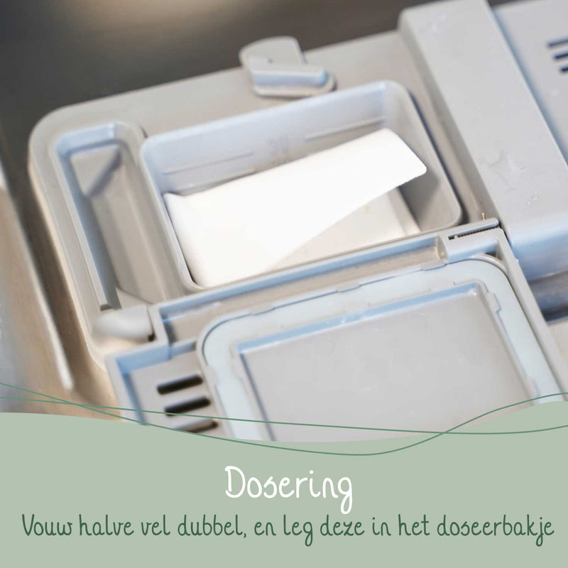 Ein Geschirrspüler-Dosierfach mit einem gefalteten Spülmaschinentab und niederländischem Text "Dosierung: Vouw halve vel dubbel, en leg deze in het doseerbakje" (Dosierung: Falten Sie die halbe Folie doppelt und legen Sie sie in das Dosierfach).