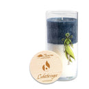 Eine wunderschön gestaltete Kerze in einem Glashalter mit blauen und weißen Schichten, der Illustration einer Frau, die Kräuter hält, und einem Holzetikett.