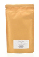 Eine stehende, braune Papiertüte mit einem weißen Etikett, auf dem „Trikatu Pulver“ und „100g“ sowie andere Produktinformationen zu lesen sind.